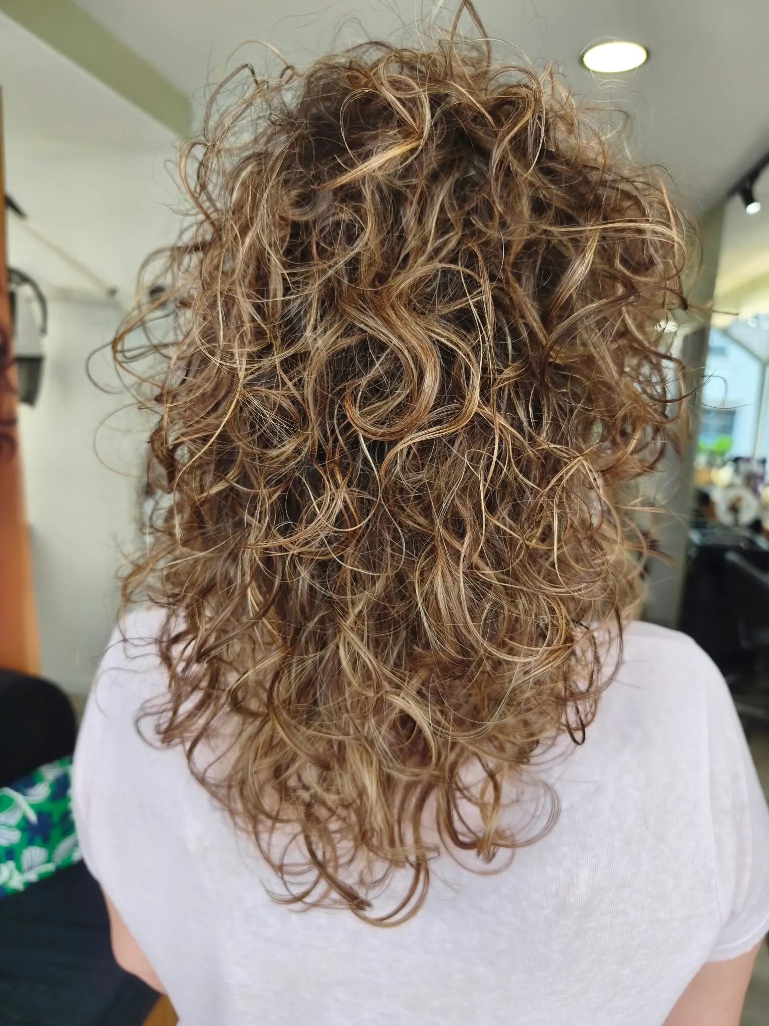 Coupe curly shag mi-longue aux boucles serrées et aux reflets blond doré