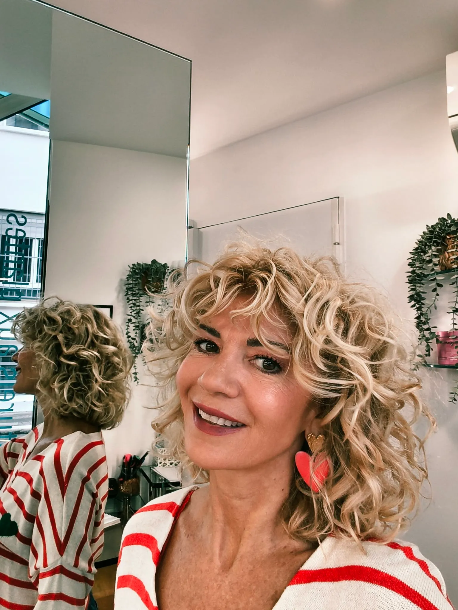 Coupe curly shag blonde très claire avec frange bouclée et racines plus foncées